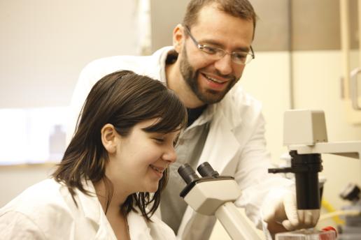Researcher and student in the lab. The student is about to look into a microscope