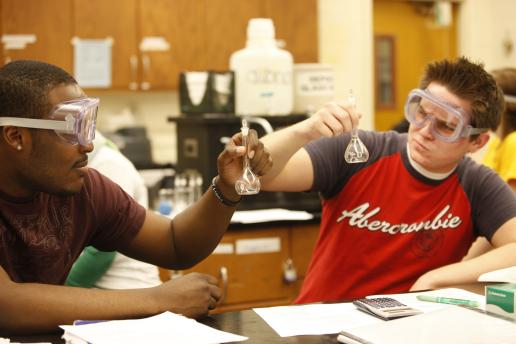 2 students working in a lab wearing goggles and holding test tubes.