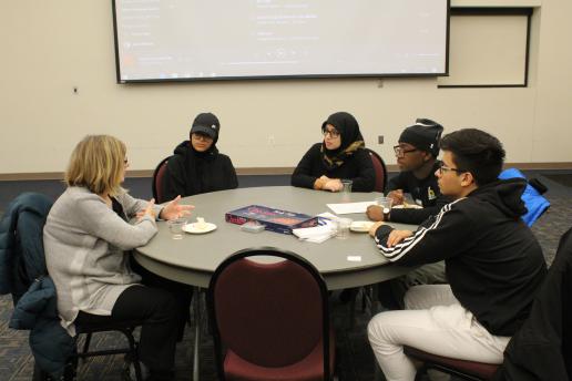 4 students and instructor holding a discussion at a round table.
