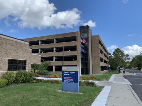 Front entrance and sign of Campus Support Services with parking structure in the background