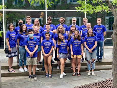 A group of students from the UM-Dearborn mathematics research experience. They are all wearing purple shirts with maize text reading, “UM-Dearborn Math REU 2021”