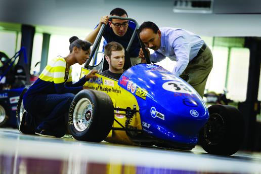 3 students and their instructor looking a SAE car
