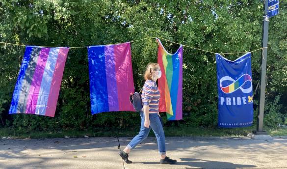 Masked student walks in front of 4 different Pride flags