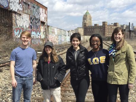 4 students standing in a railyard with background walls all covered in graffiti