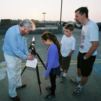 Researcher setting up portable telescope for 2 kids and father to look into