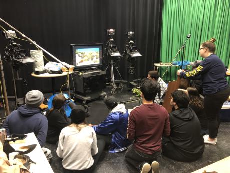 Students viewing tv monitor in studio with green wall