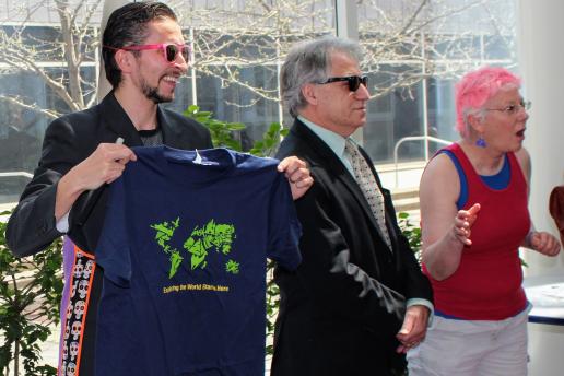 3 people presenting with one man holding a t-shirt that has a map of the world on it.
