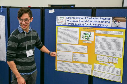 Student sharing research in front of his poster.