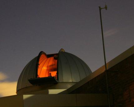 Open observatory dome with orange light escaping the dome against night sky