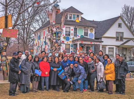 Group photo of people standing in front of a house in the Heidleburg project of Detroit