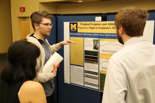 Student presenting his research poster to 2 people