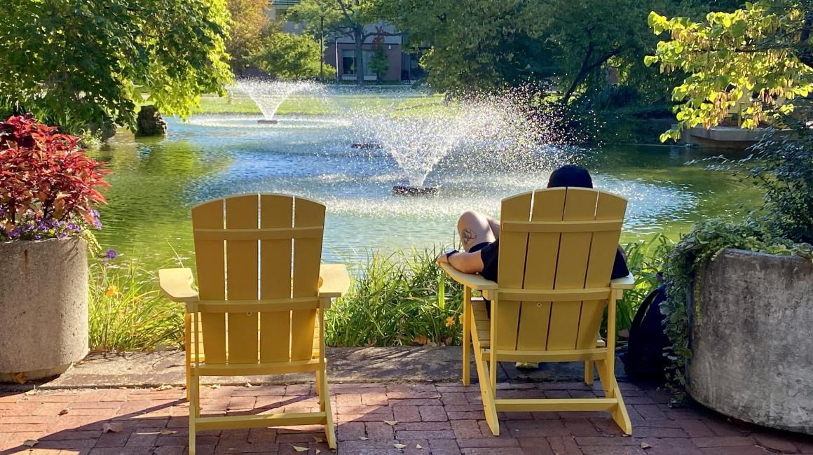 A postcardlike shot of someone relaxing in the new yellow Adirondack chairs near Chancellor's Pond in late summer.
