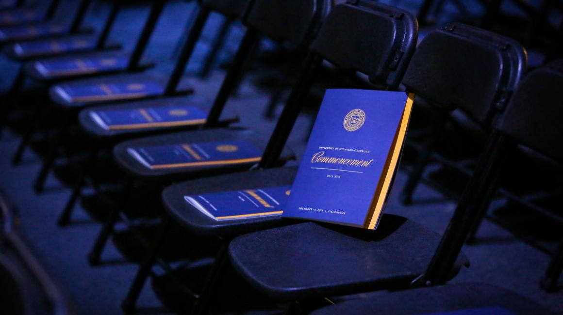 A row of empty chairs with commencement programs sitting on them.