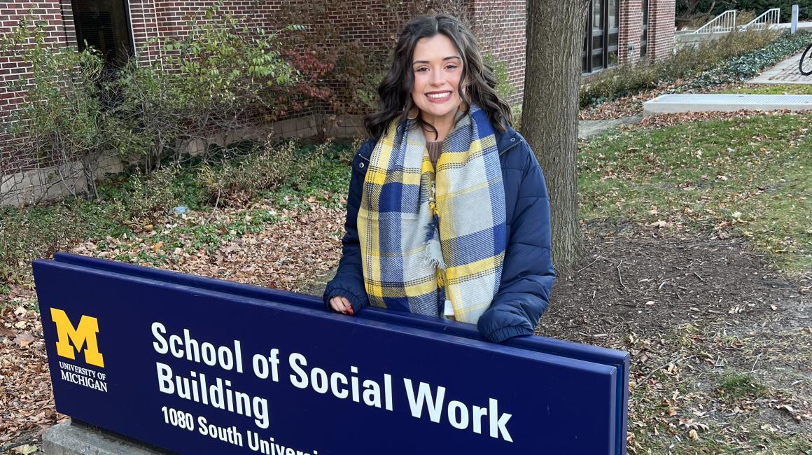UM-Dearborn senior Riley Day stands behind the U-M School of Social Work Building nameplate on a winter day on the Ann Arbor campus.