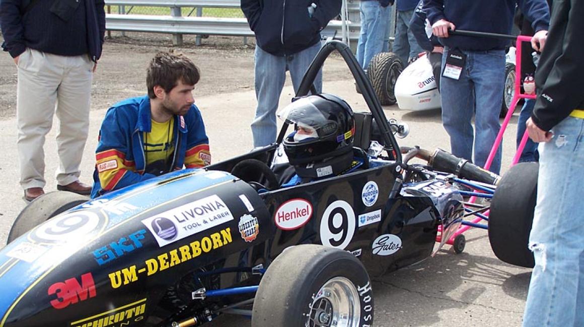 Roland Dibra crouches by the FSAE team race car