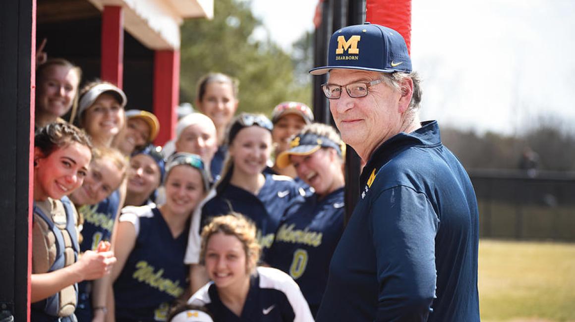 Kirk Philipich wearing Michigan baseball cap with female student-athletes standing behind him.