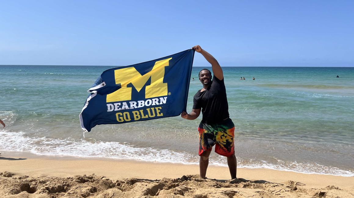 Student holding UM-Dearborn flag on the beach of Puerto Rico