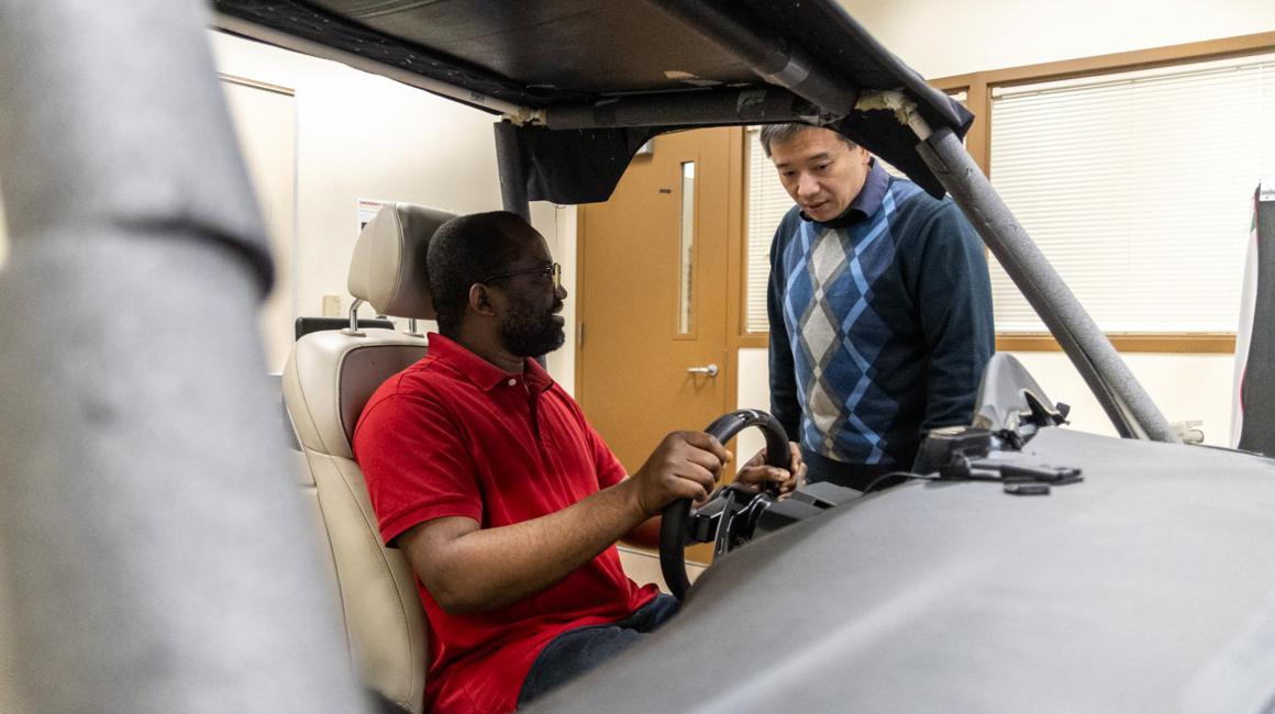 Associate Professor of Industrial and Manufacturing Systems Engineering Bochen Jia talks with a graduate student in a driving simulator.