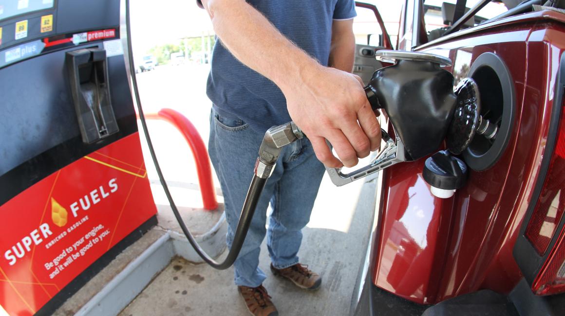 A white man’s hand is seen holding a gas pump and filling the tank of a red vehicle.