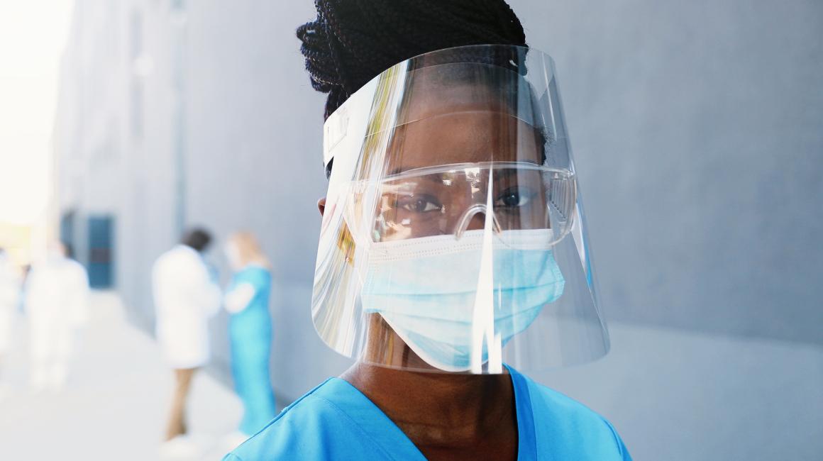 A Black woman wearing a protective face mask and shield.