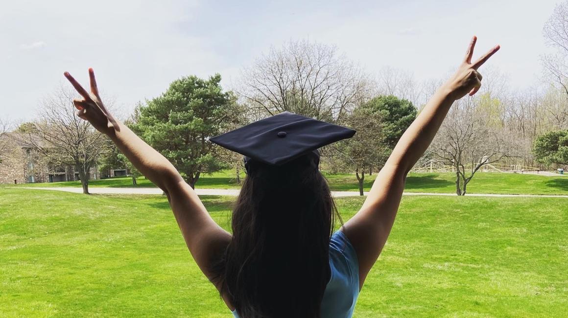 A woman in a graduation cap raising her hands in the air.