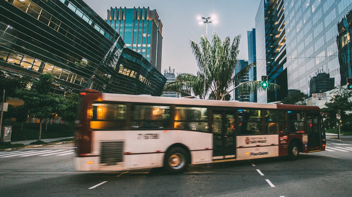 An evening photo of downtown Detroit with a bus moving through an intersection. The white-red bus is out of focus.