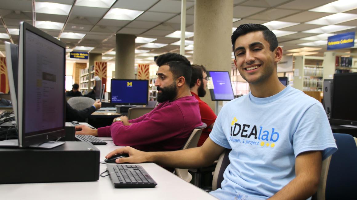 Ali Almehdi is a young Arab man with slicked black hair. He and another man sit in front of computers in the library.