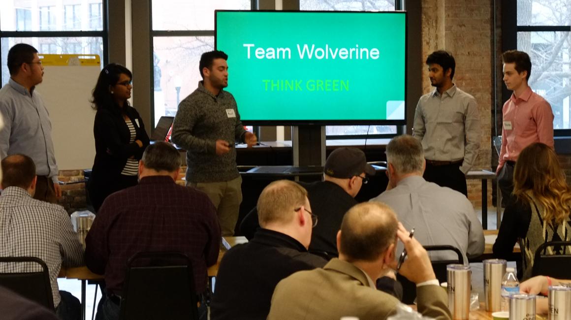 Presentation of 5 people in front of a screen that reads: Team Wolverine Think Green.