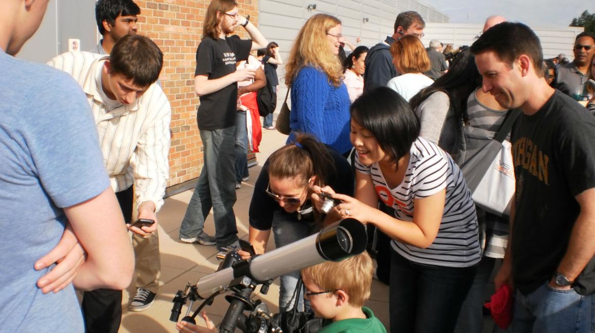 Public observation at the Observatory. Parents and children gather around a telescope outside.