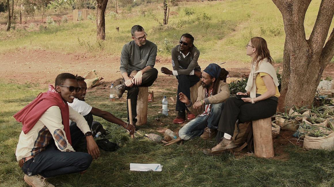 A group of students and Rwandan people sit outside of a trail in Rwanda.