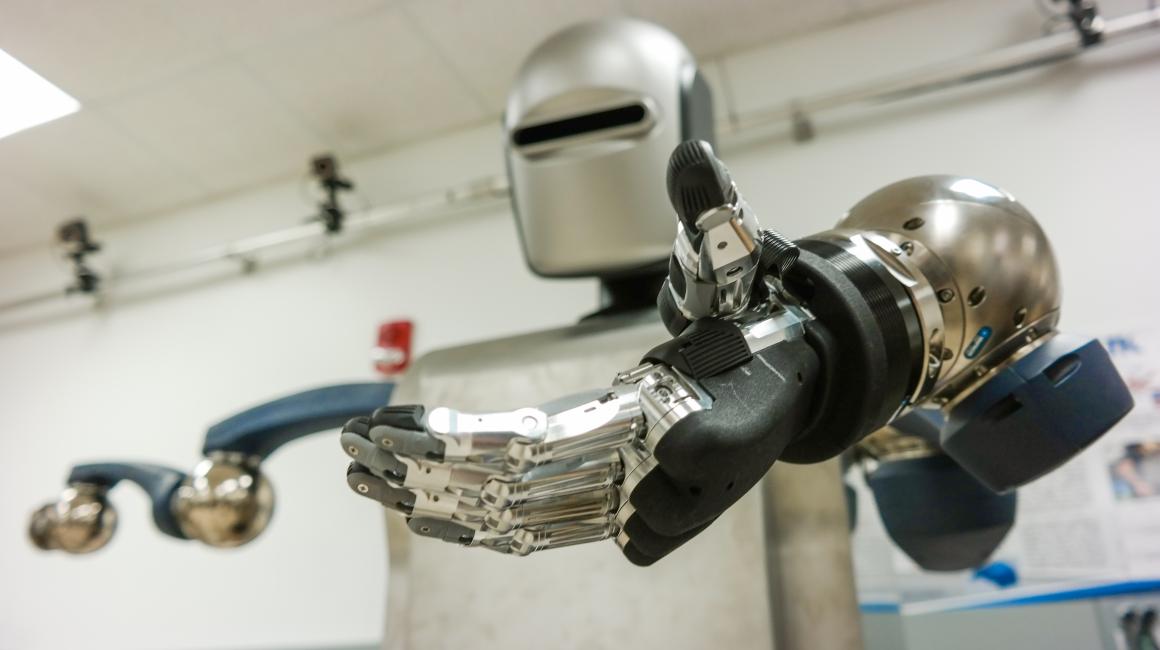 A silver humanoid robot holding out a mechanical “hand” towards the camera.