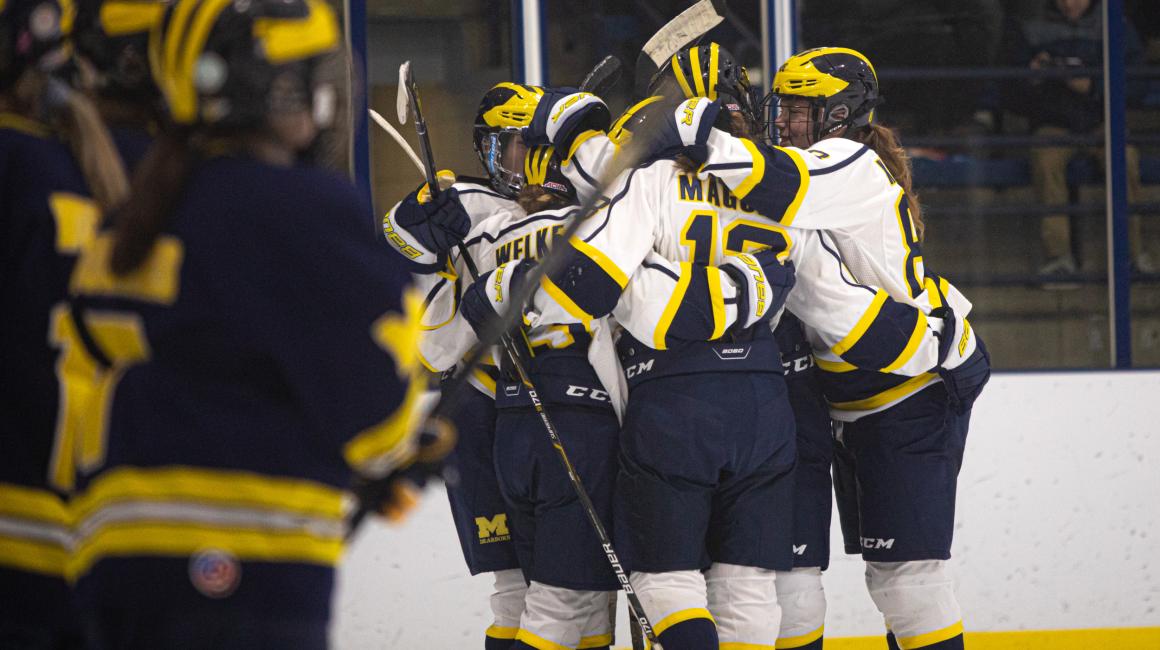 The UM-Dearborn women’s ice hockey team hugging and huddling on the ice.