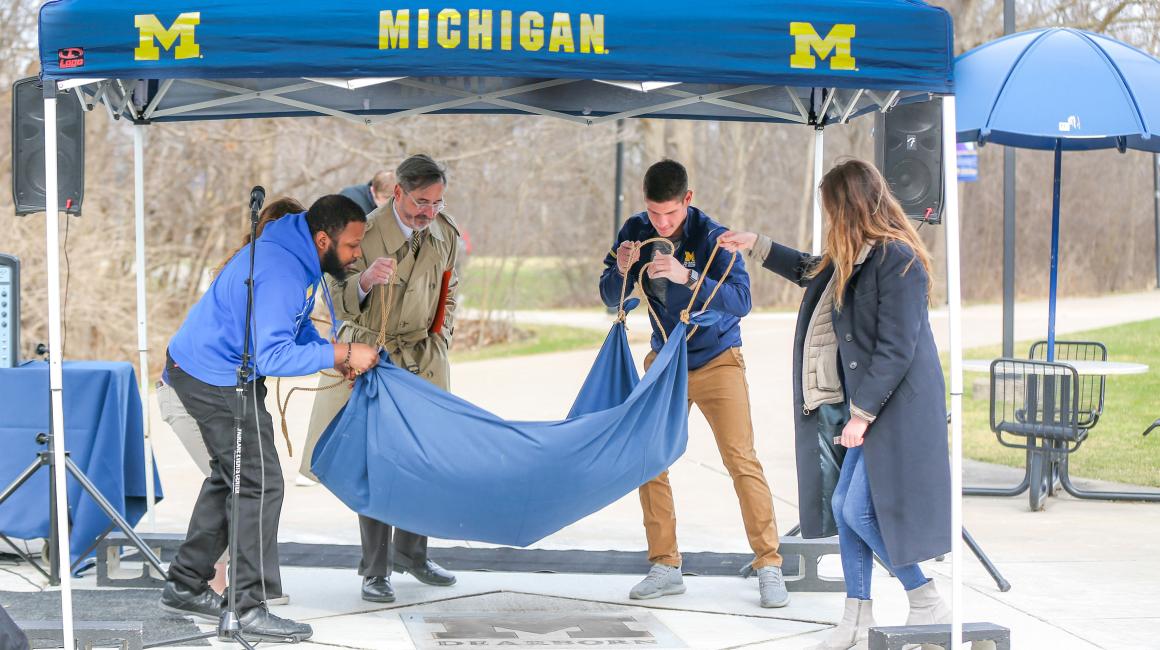 Chancellor Domenico Grasso helps three students unveil a granite and bronze UM-Dearborn Block M outside of the University Center.