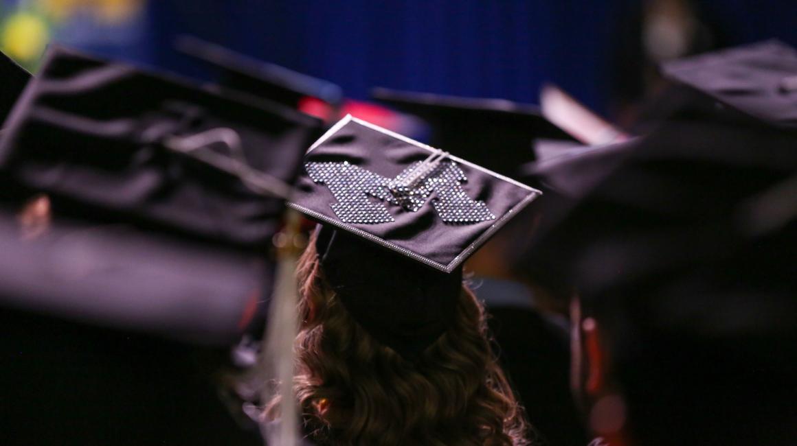 A woman wearing a graduation cap with a rhinestoned varsity-style 'M'