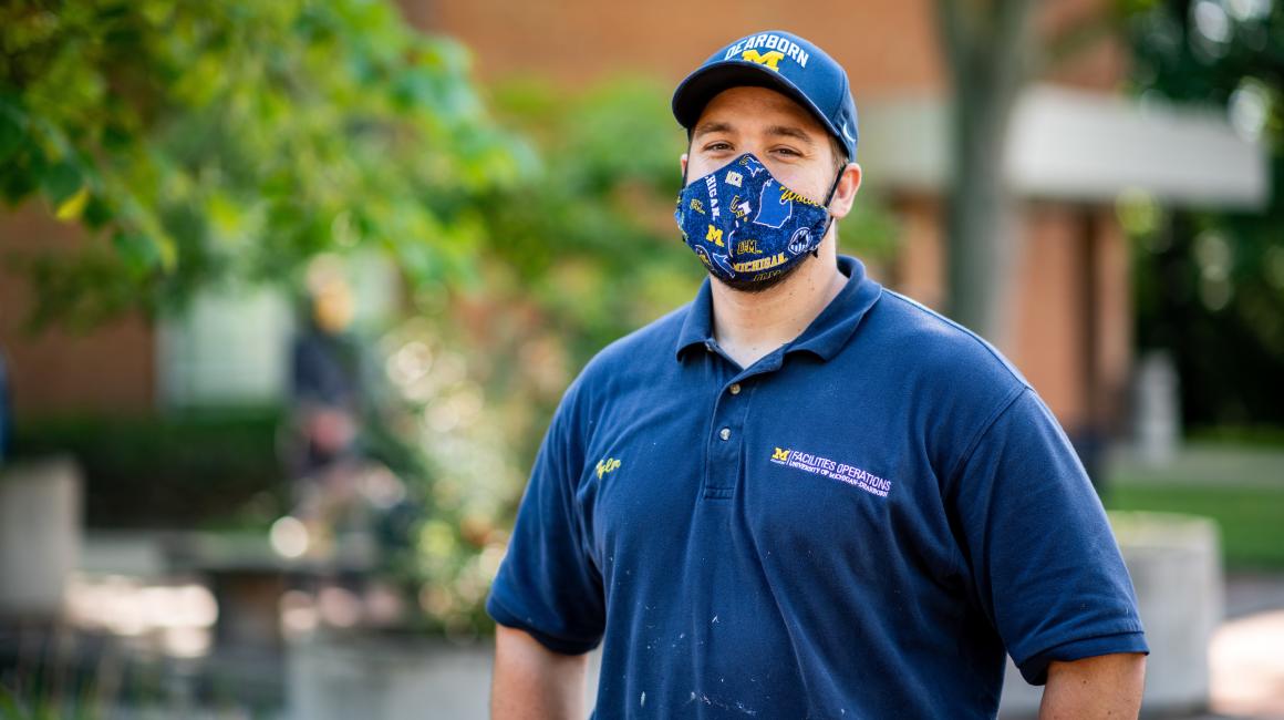 Tyler Petee is a middle-aged white man with short, blond hair. He is wearing his UM-Dearborn Facilities Operations polo t-shirt, a UM-Dearborn face mask, and UM-Dearborn baseball cap.