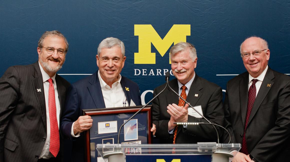 Mark Schlissel, Ronald Weiser, Tony England, and Daniel Little stand in front of a podium holding the Weisers’ gift for the ELB.