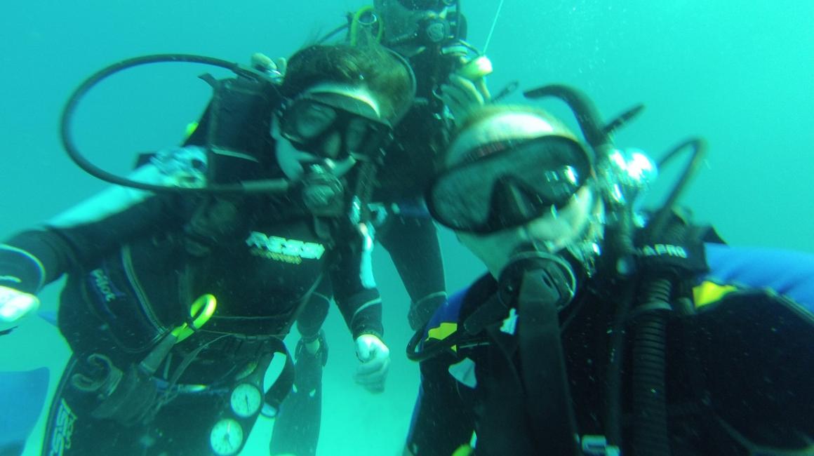 Three students in a selfie underwater. They are wearing scuba diving gear.