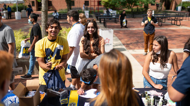 Smiling students line up to get swag at a welcome back to campus event on a sunny day in September.