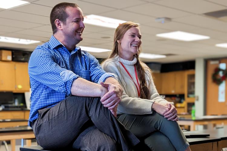 Natalie Fowler and teacher Peter Kohnen sit on desks in their empty high school classroom.