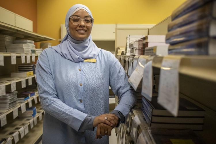 New Bookstore Manager Lulu Owens-Berry stands for a photo in between stacks of textbooks on shelves.