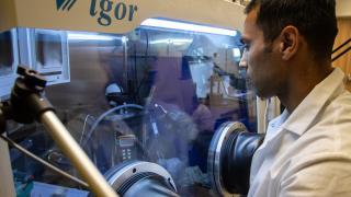 Wearing a white lab coat, graduate student Hossein Abbasi manipulates equipment inside a plastic chamber in the lab of battery researcher Assistant Professor Lei Chen.