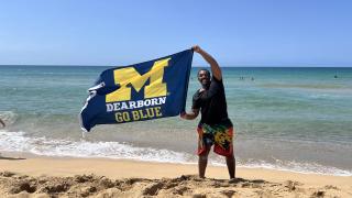 Student holding UM-Dearborn flag on the beach of Puerto Rico