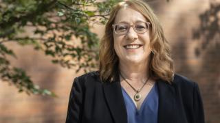 Woman with glasses, standing near tree, smiling