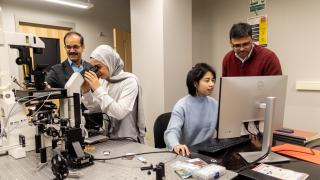 Flanked by microscopes and computers, Associate Professor of Biology Kalyan Kondapalli and Assistant Professor of Physics Suvranta Tripathy work with two female graduate students in a biology lab.