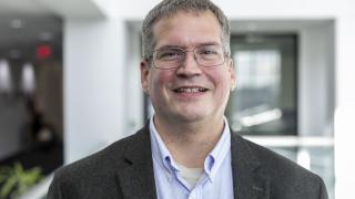 Headshot of smiling man with glasses in sportcoat