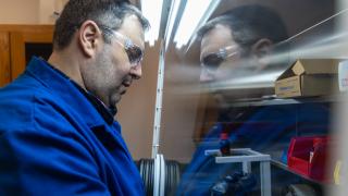 A university researcher in a blue coat and safety glasses conducts chemistry experiments in his lab