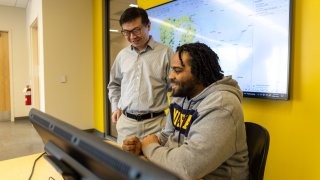 A smiling student and a professor look at data on a computer screen