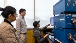 Three researchers look at battery equipment in a university research lab