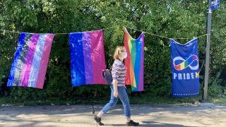 Masked student walks in front of 4 different Pride flags